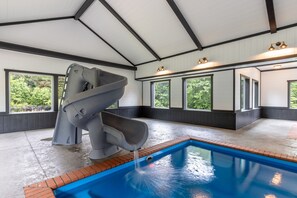 A covered swimming pool with a slide, large windows, and a ceiling with exposed beams. - Black Eagle Lodge -  Unique - 8 Bedrooms - 2 Pools (Logan)