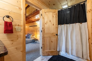 Un intérieur en bois avec une porte donnant sur une chambre, une serviette rouge accrochée à un anneau et un rideau noir et blanc.