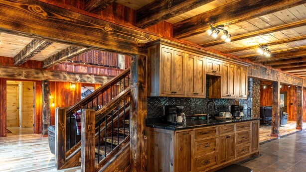 A spacious kitchen with wooden cabinets, a central island, and a staircase leading to another level. - Black Eagle Lodge -  Unique - 8 Bedrooms - 2 Pools (Logan)