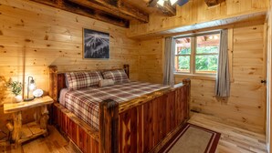 A wooden cabin bedroom with a bed, a nightstand, a lamp, a window with curtains, and a ceiling fan. - Black Eagle Lodge -  Unique - 8 Bedrooms - 2 Pools (Logan)