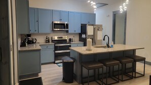 A modern kitchen with grey cabinets, stainless steel appliances, a central island with bar stools, and pendant lighting. - Newly built, Pool, Pier, Elec. Golf Cart, Elevator, Sleep 10, 2 min walk to surf (Navarre)