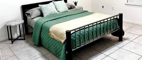 Una cama con colcha verde, una mesita de noche y una pequeña planta en maceta.