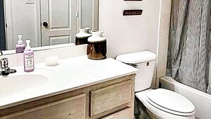 Une salle de bain avec un lavabo blanc, un miroir, des toilettes et un rideau de douche.