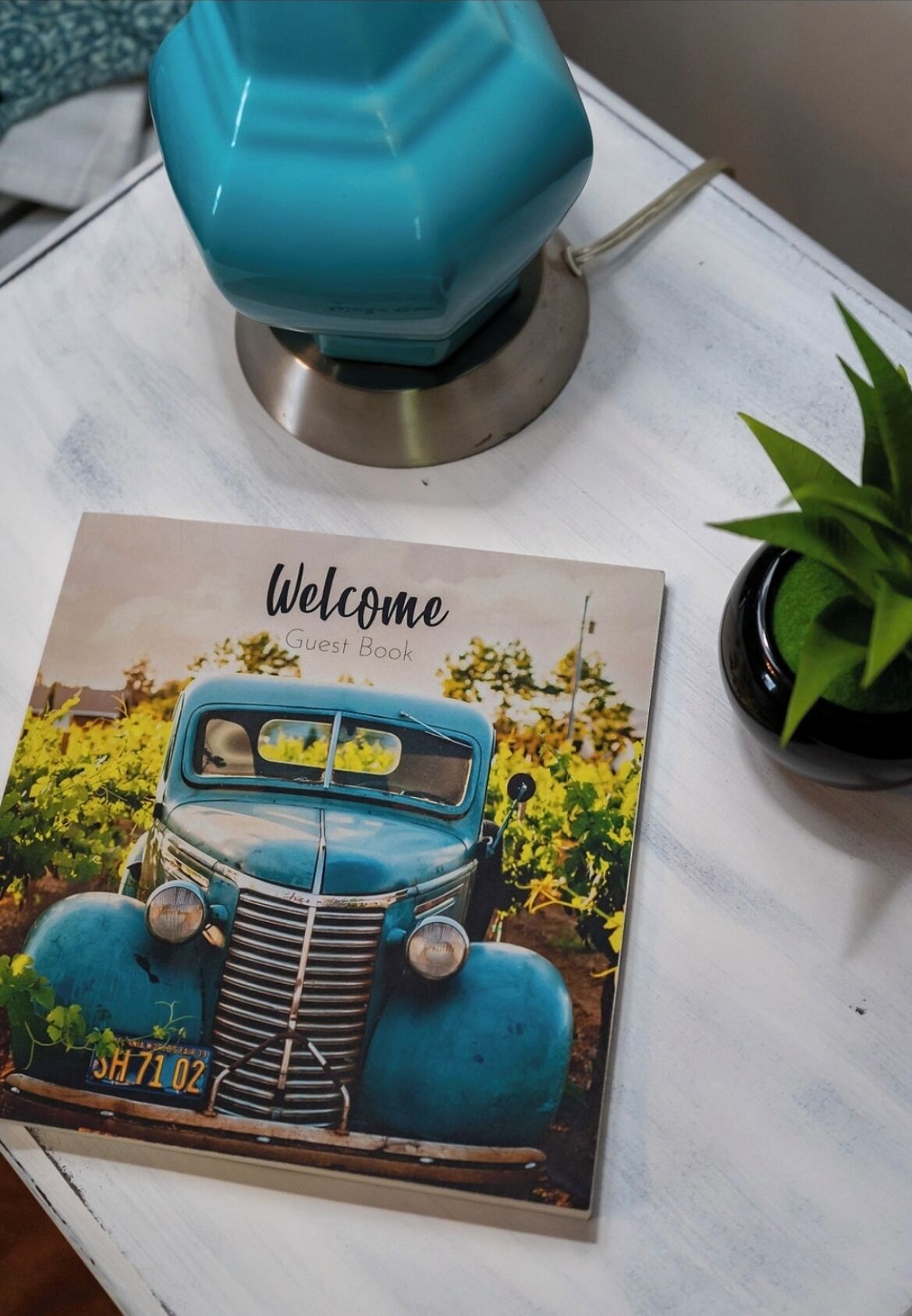A vintage car poster with the text "Welcome Guest Book" on a white table.