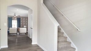 Un pasillo con una escalera, piso de madera y un comedor con sillas y una mesa.