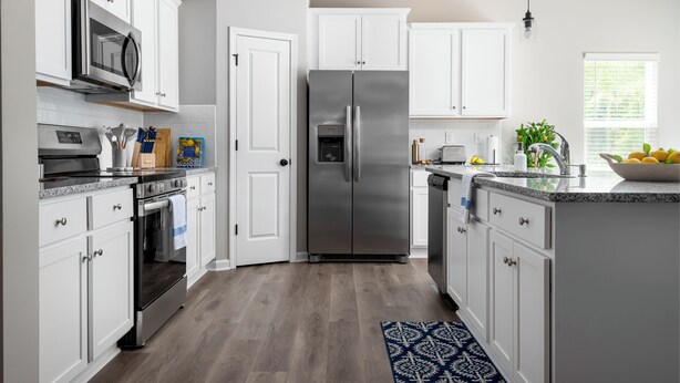 Una cocina moderna con armarios blancos, electrodomésticos de acero inoxidable y una alfombra estampada.