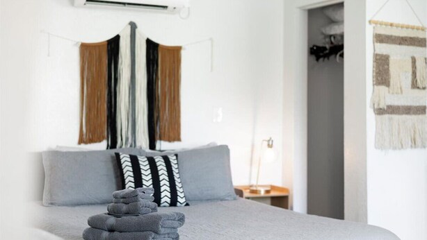 A neatly made bed with grey bedding and a stack of folded towels. - 1BR/1BA Design District Cottage - 8 Min drive from Downtown WPB (West Palm Beach)