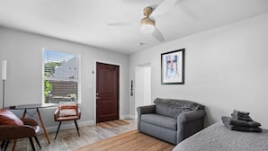 A modern living room with a gray sofa, a brown leather chair, a small table, and a ceiling fan. - 1BR/1BA Design District Cottage - 8 Min drive from Downtown WPB (West Palm Beach)