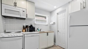 A kitchen with white cabinets, a microwave, a stove, a dishwasher, and a refrigerator. - 1BR/1BA Design District Cottage - 8 Min drive from Downtown WPB (West Palm Beach)