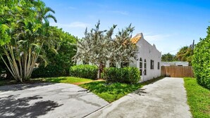 A residential house with a white exterior, a sloped roof, and a front yard with a tree and shrubs. - 1BR/1BA Design District Cottage - 8 Min drive from Downtown WPB (West Palm Beach)