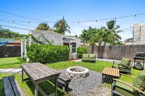 Relax in a serene backyard oasis with a fire pit, wooden table, and lush greenery.