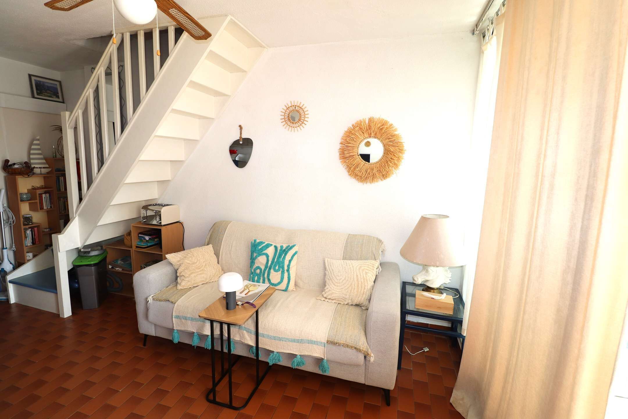 Uma sala de estar com sofá, mesa de centro, abajur, estante e escada.