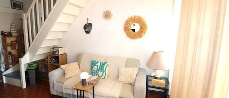 Uma sala de estar com sofá, mesa de centro, abajur, estante e escada.