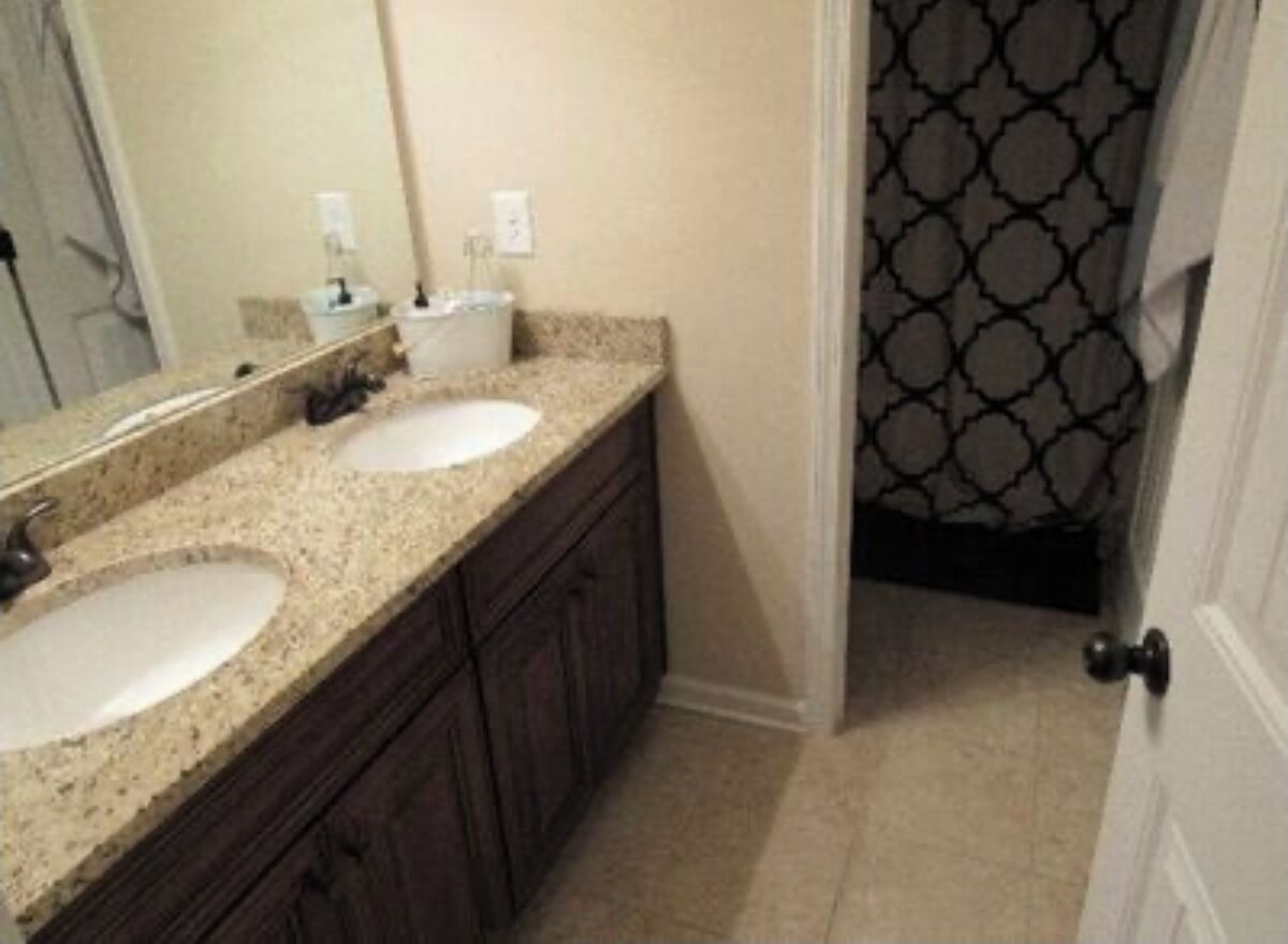 Une salle de bain avec deux lavabos, un miroir et une porte donnant sur une pièce aux motifs décoratifs.