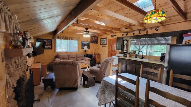 Interior acolhedor de uma cabana, com sala de estar, cozinha e uma parede de pedra.