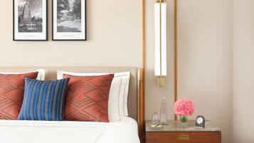 Habitación de hotel ordenada con cama, almohadas, una mesita de noche, una lámpara y dos cuadros en la pared.