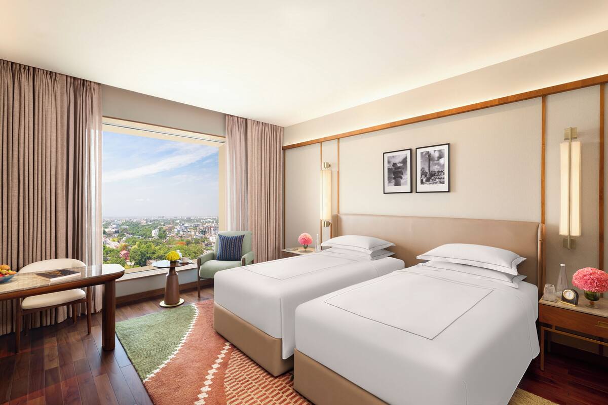 Een hotelkamer met twee bedden, een eettafel, een stoel, een klein tafeltje met een vaas en uitzicht op de stad.