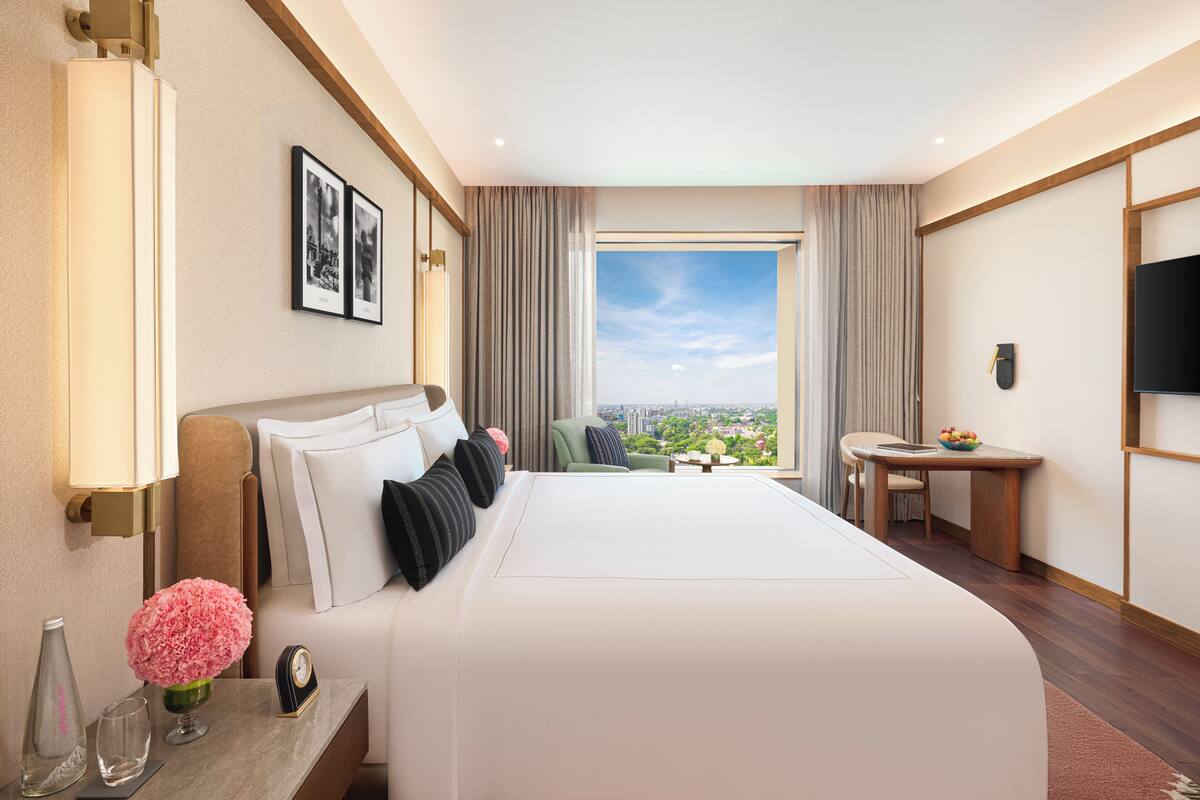 Een hotelkamer met een groot bed, een bureau, een stoel, een televisie en uitzicht op de stad.