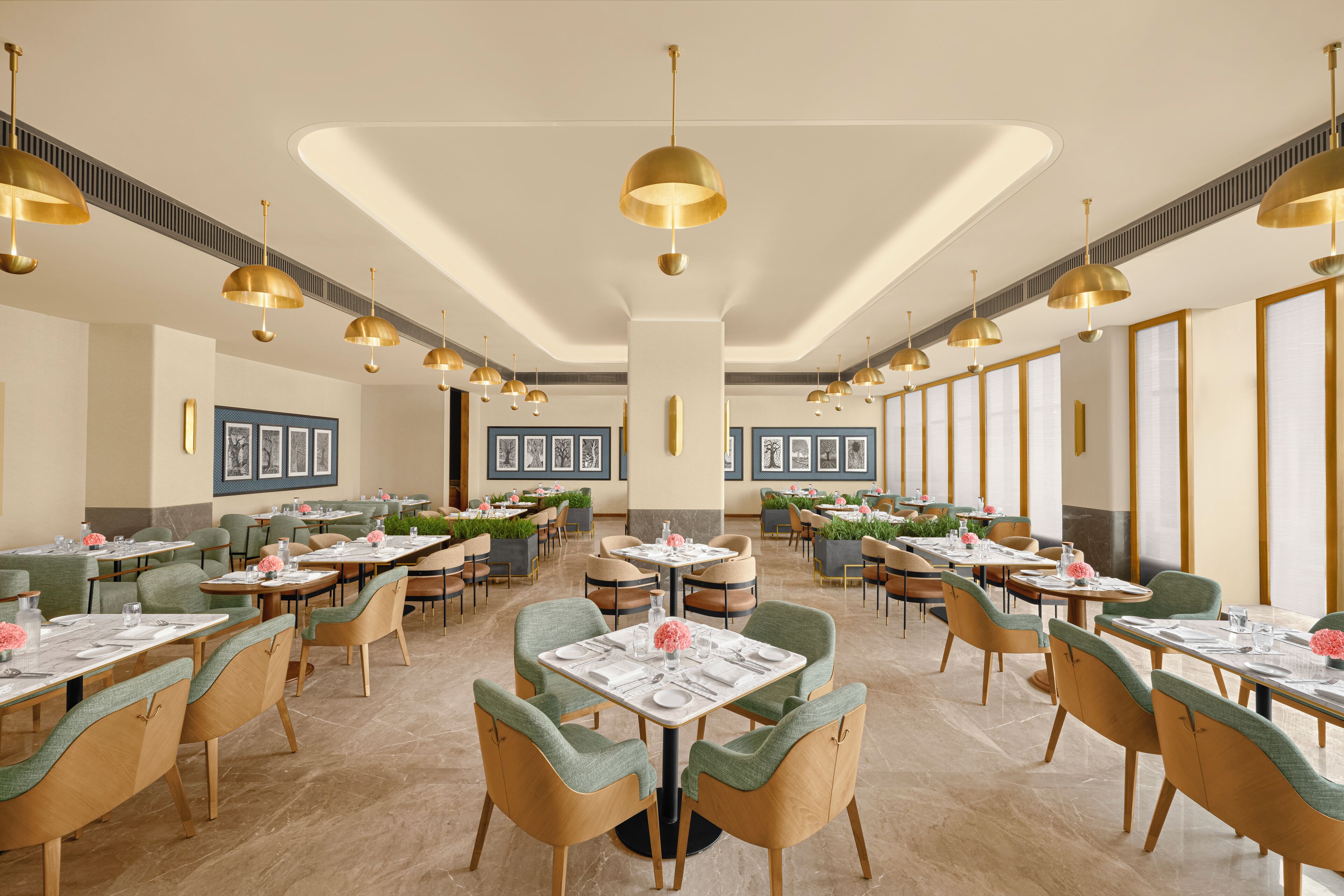 A spacious dining area with multiple tables and chairs, featuring a modern design with gold pendant lighting and framed artwork on the walls.