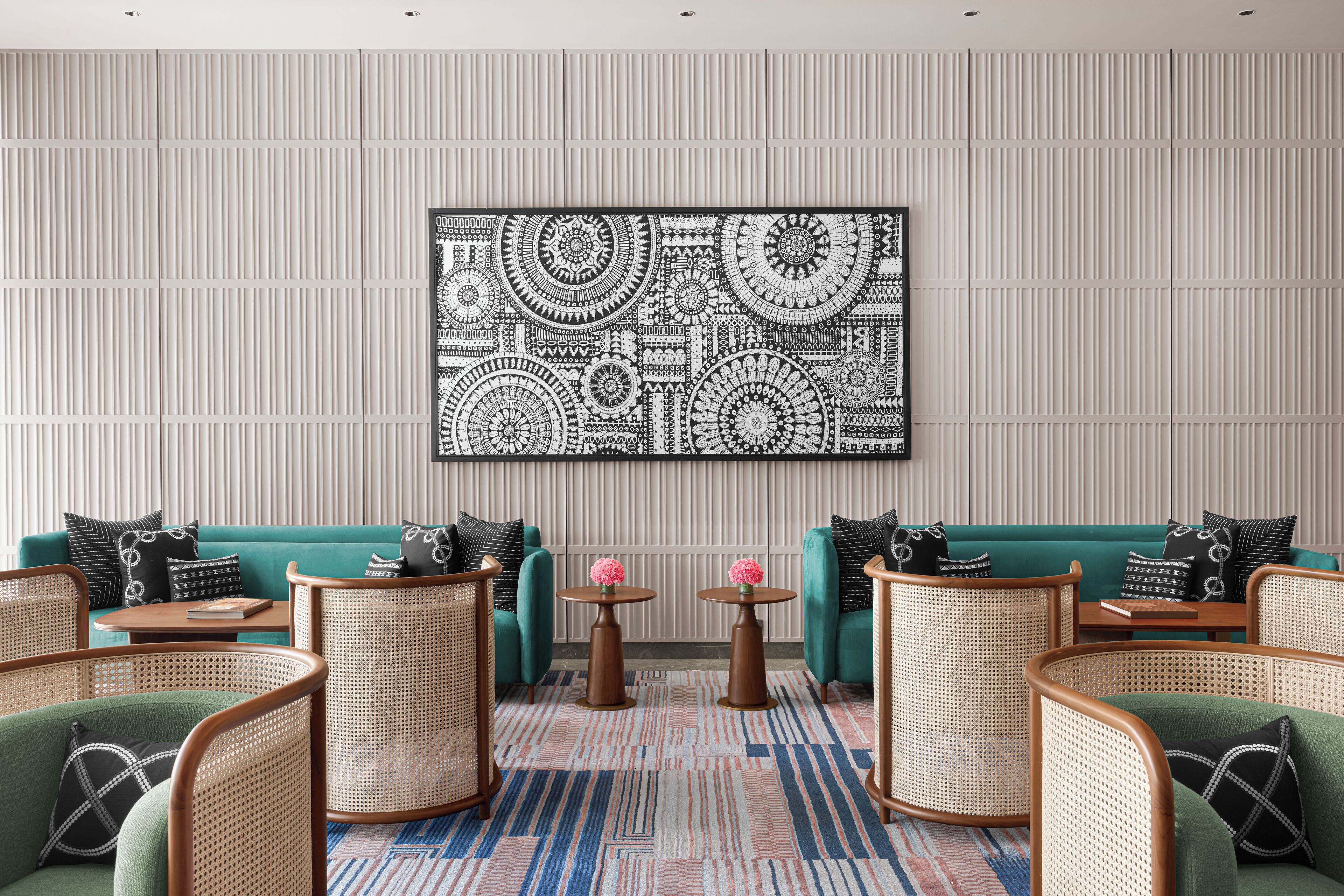 A modern living room with teal sofas, wicker chairs, and a patterned wall art piece.
