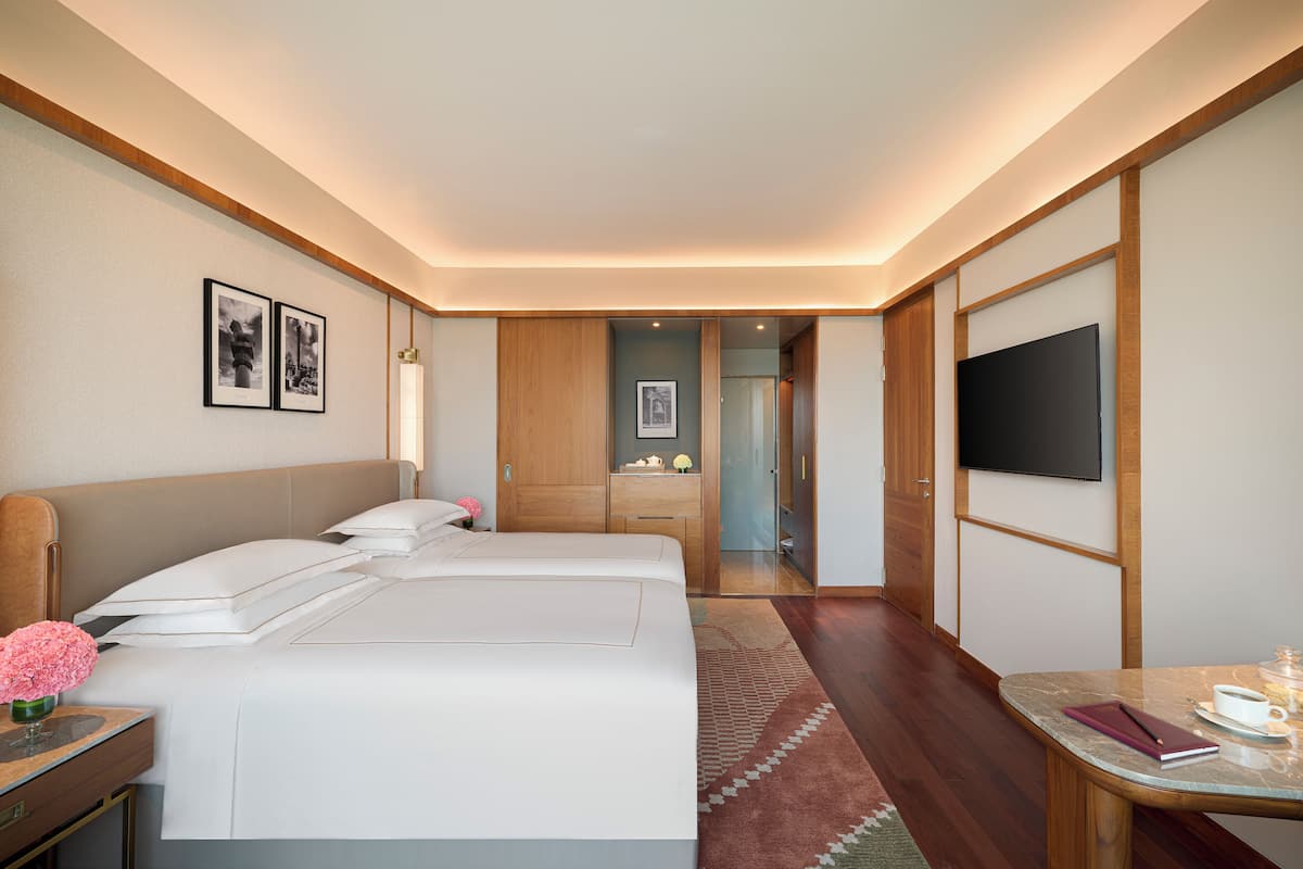 Hotelkamer met twee bedden, een televisie, een bureau met een kopje en een notitieboekje, en een badkamer die door een open deur zichtbaar is.
