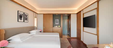 A hotel room with two beds, a TV, a desk with a cup and a notebook, and a bathroom visible through an open door.