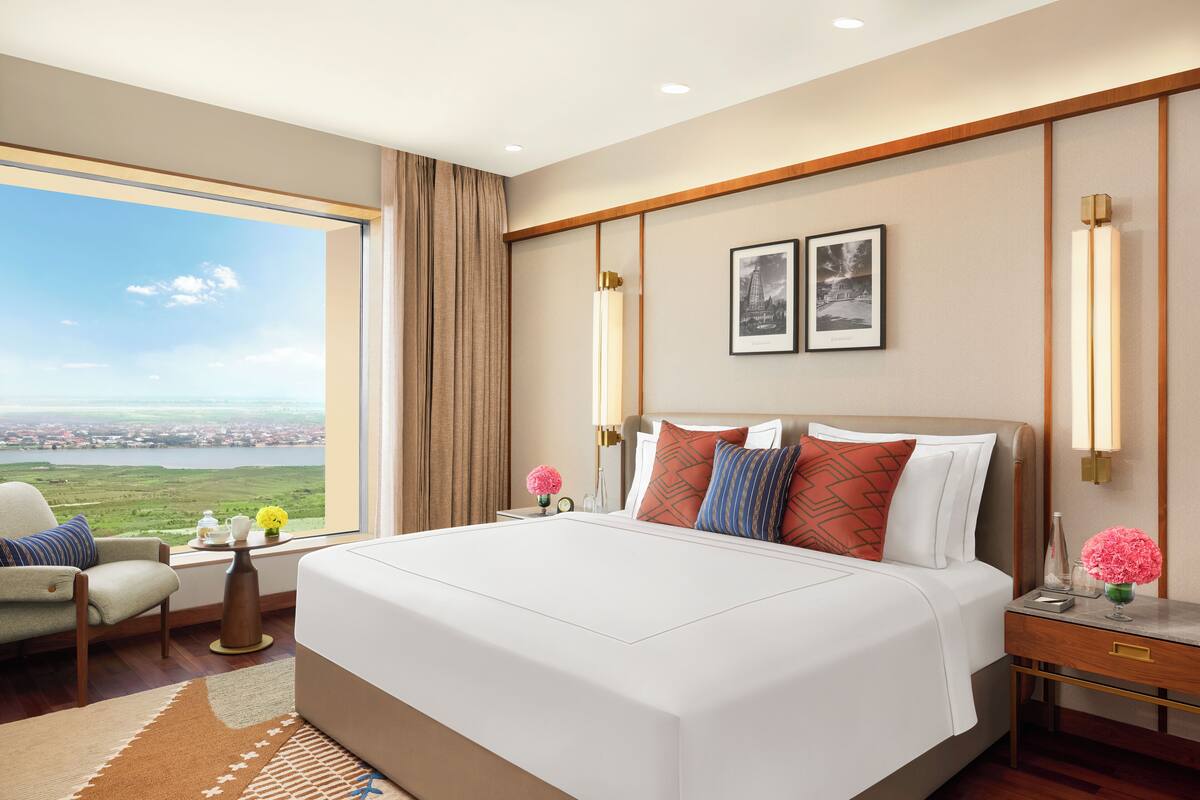 Hotelkamer met een groot bed, uitzicht op het landschap, een stoel, nachtkastje en een lamp.