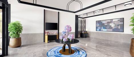 Un vestíbulo moderno con piso de mármol, una mesa redonda con alfombra azul y marrón, y plantas en macetas.