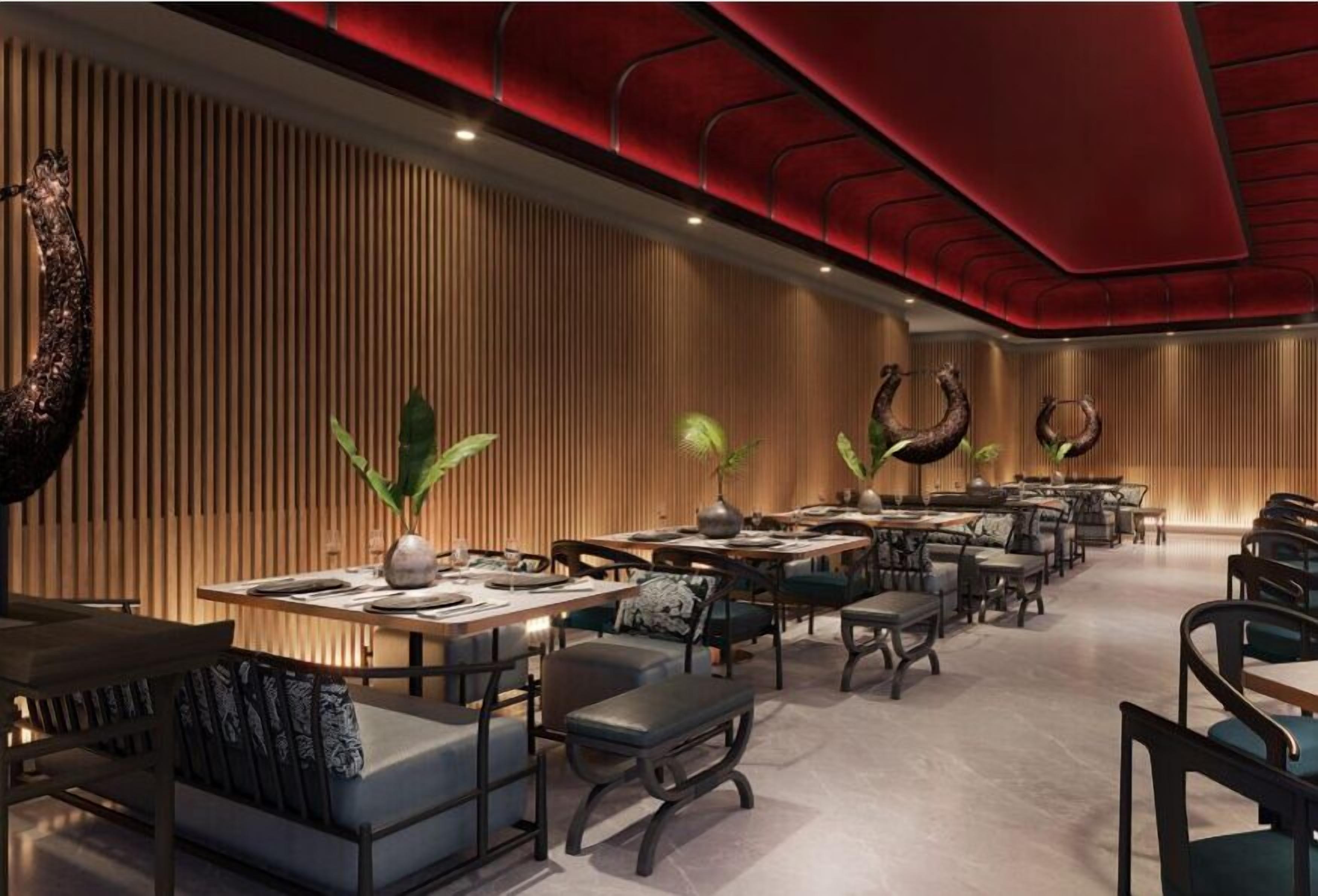 Un restaurante moderno con paneles de madera, plantas verdes y techo rojo. Las mesas y sillas están dispuestas para comer.