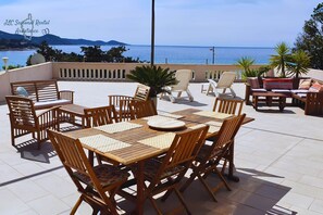 An outdoor patio with wooden furniture, including tables and chairs, overlooking a body of water. - Villa U rustincu (Pietrosella)