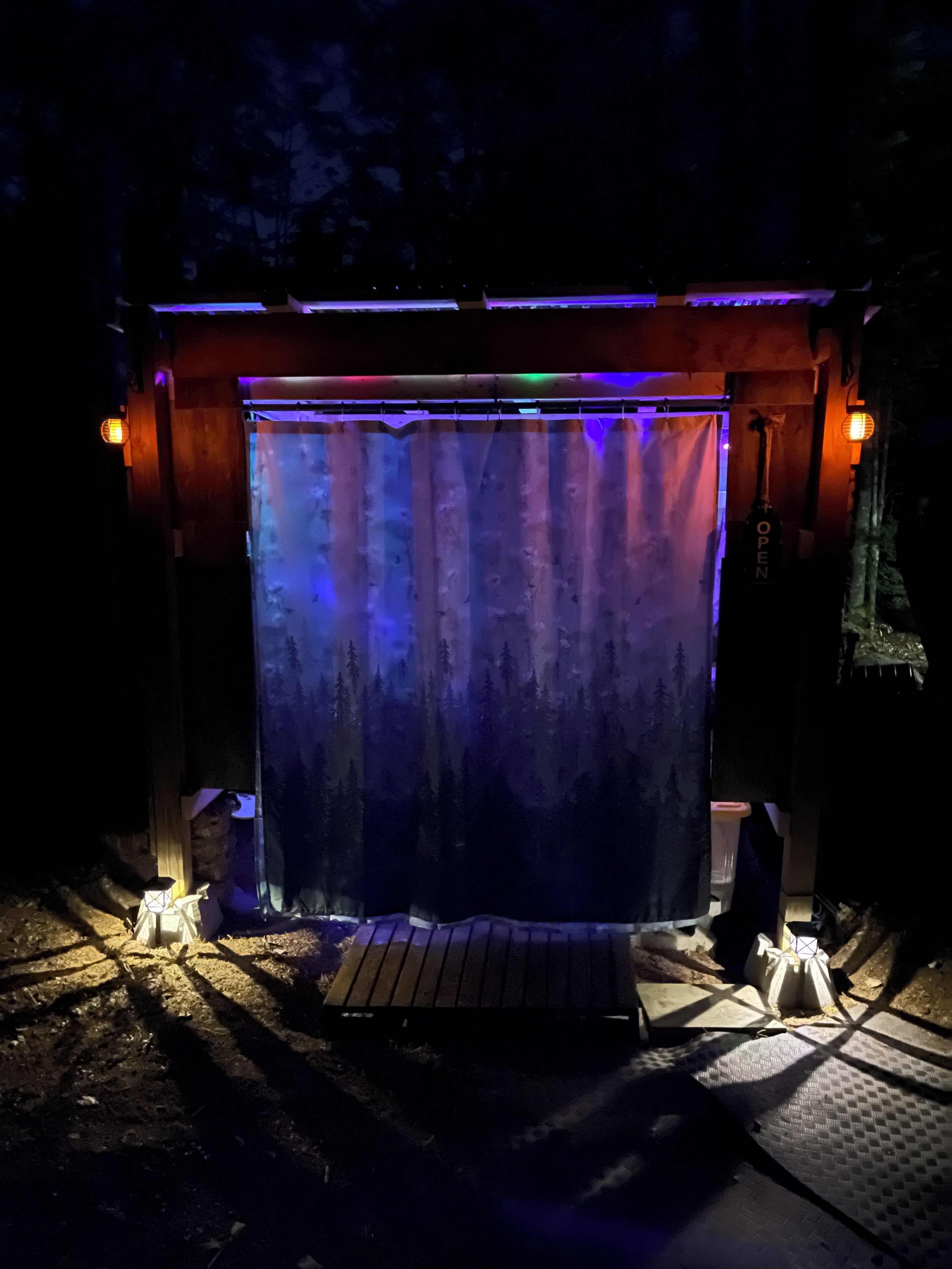 A covered outdoor area with a wooden deck, a curtain, and a sign that reads "OPEN".