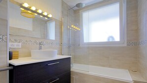 A modern bathroom with a large mirror, a white sink, a dark vanity, a shower with a glass door, and a bathtub. - Appartement des Chênes - Welkeys (Anglet)