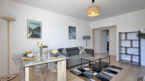 A modern living room with a glass dining table, sofa, and a bookshelf. - Appartement des Chênes - Welkeys (Anglet)