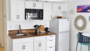 A modern kitchen with white cabinets, a stainless steel sink, and a black microwave.