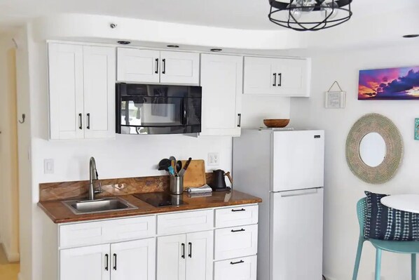 A modern kitchen with white cabinets, a stainless steel sink, and a black microwave.