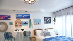 A bedroom with a bed, a small table, two bar stools, and artwork on the walls.