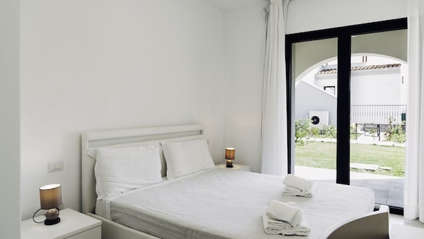 Een hotelkamer met een bed, een nachtkastje met een lamp en uitzicht op het buitengebied door een glazen deur.