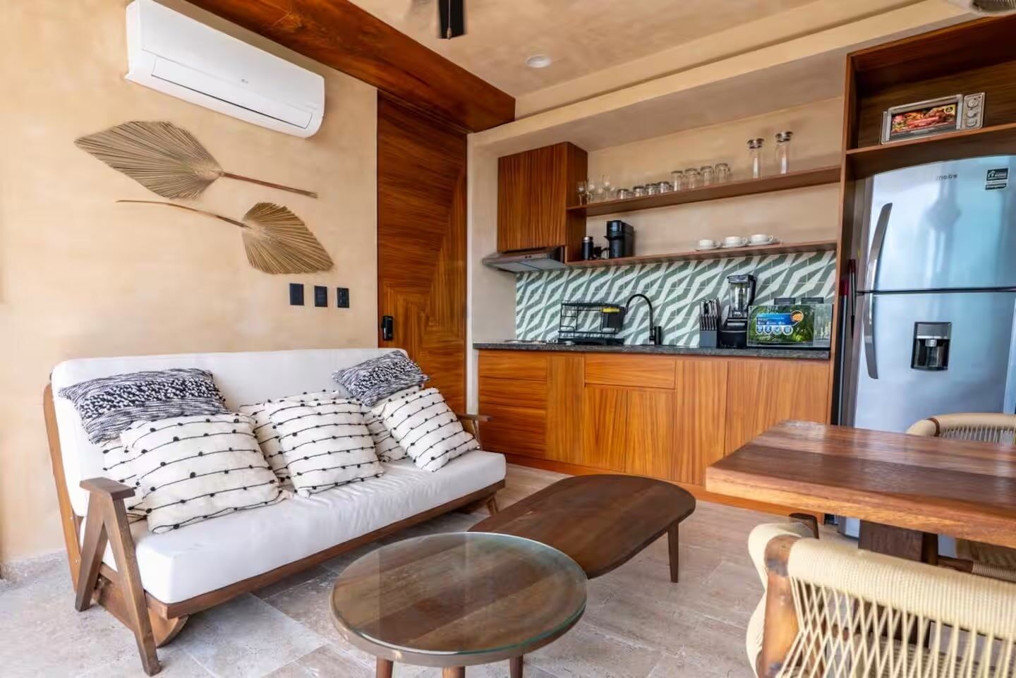 A compact living space with a sofa, a glass table, a kitchen area with a refrigerator, and a coffee machine.