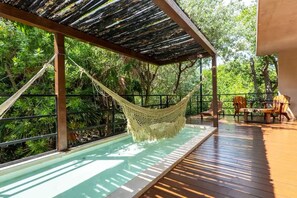 Una hamaca sobre una piscina, terraza de madera y sillas.