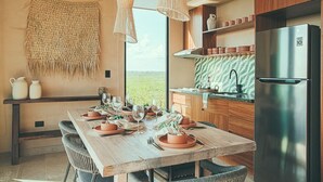 A modern kitchen with a large wooden table set for dining, a stainless steel refrigerator, and a view of the outdoors. - BT Homes - Tankah Bay (Tulum)