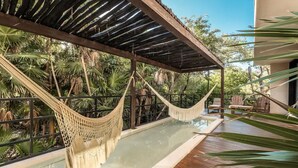 A hammock over a pool with a wooden deck and outdoor furniture, surrounded by lush greenery. - BT Homes - Tankah Bay (Tulum)