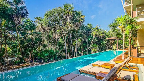 A pool with lounge chairs and a wooden deck, surrounded by lush tropical vegetation. - BT Homes - Tankah Bay (Tulum)