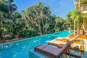 A pool with lounge chairs and a wooden deck, surrounded by lush tropical vegetation. - BT Homes - Tankah Bay (Tulum)