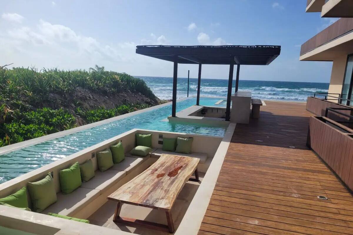 A poolside area with a wooden deck, a lounge with green cushions, and a view of the ocean.