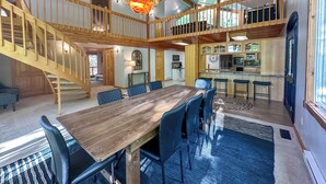 Un comedor amplio con una mesa de madera y sillas azules, una cocina con barra y una escalera de madera que conecta dos niveles.