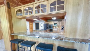Una cocina con encimera de granito, armarios de madera y tres taburetes de bar.