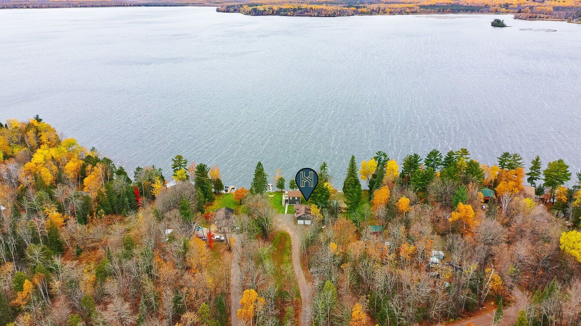 Une vue sur le lac, avec le feuillage automnal, un ciel dégagé et une petite cabane, dont on aperçoit le chemin qui y mène.