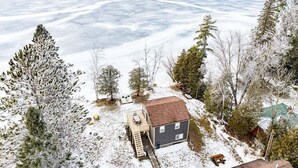 Una casa con terraza y un pequeño porche, rodeada de árboles cubiertos de nieve y un lago helado.