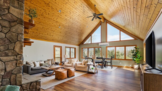 A spacious living area with a stone wall, wooden ceiling, and large windows offering views of the outdoors.