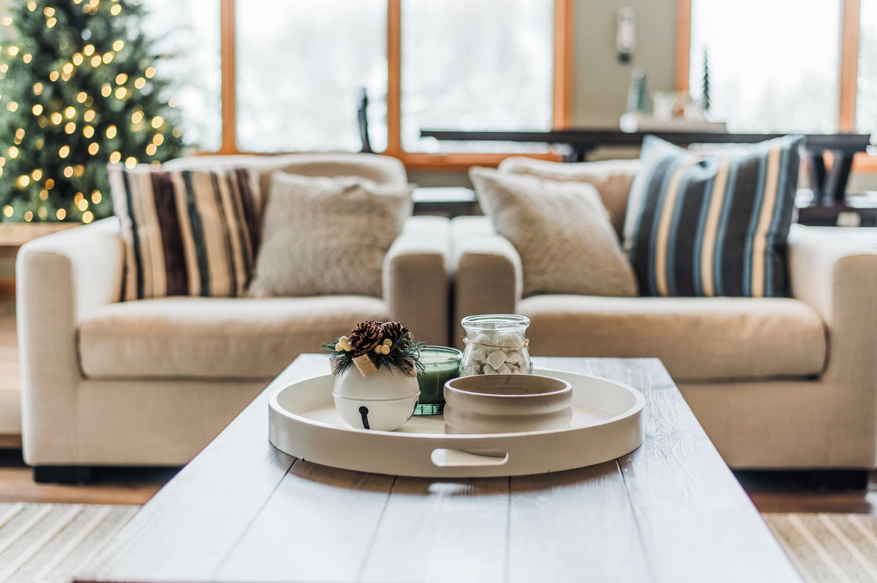 Un salon chaleureux avec un canapé beige, une table basse agrémentée d’objets décoratifs et un sapin de Noël en arrière-plan.
